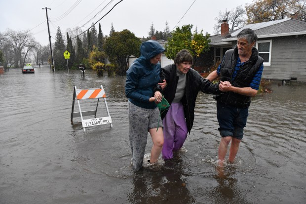 Katie Leonard, of Pleasant Hill, left, assists Scott Mathers, of Pleasant Hill, as they rescue Mathers' mother Patsy Costello, 88, of Pleasant Hill, after being trapped in her vehicle for over an hour on Astrid Drive in Pleasant Hill, Calif., on Saturday, Dec. 31, 2022. Costello drove her car on the flooded street thinking she could make it when it stalled in the two feet of water. After two hours the water had receded about a foot making it easier to rescue her. Police were called but stood by and watched after calling in a tow truck to help pull the car out of the water. Nurse Katie Leonard, of Pleasant Hill, lives down the block used her kayak to bring Costello hot tea, blankets, food and a phone to call a friend. (Jose Carlos Fajardo/Bay Area News Group)