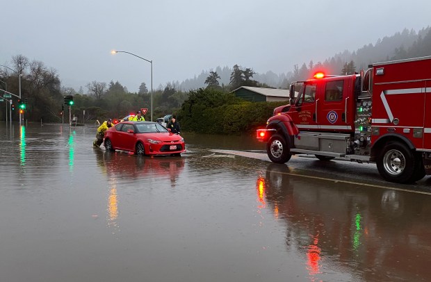 Rescue crews push Ben Lomond resident Julie Armstrong, 76, to safety after her car stalled out in the intersection of Graham Hill and Mount Hermon roads in Felton after the San Lorenzo River flooded early in the morning of Jan. 9, 2023. (John Woolfolk/ Bay Area News Group)