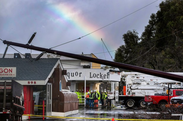 Utility crews huddle under an overhang studying a fallen power pole knocked down by the storm on Lincoln Avenue in San Jose, Calif., Tuesday, Jan. 10, 2023. (Karl Mondon/Bay Area News Group)