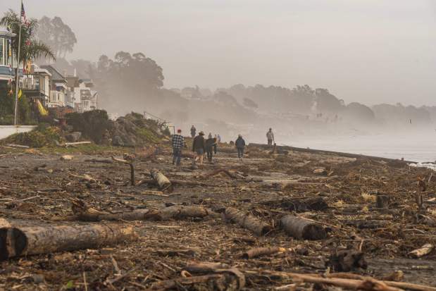 People walk on Rio Del Mar beach, covered with storm debris, in Aptos, California on January 12, 2023. (Photo by Nic Coury/AFP via Getty Images)