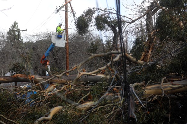 A PG&E employee works on damaged utility lines along Sandy Road on Sunday, Jan. 8, 2023, in Castro Valley, Calif. A large eucalyptus tree fell Saturday afternoon severely damaging a home, trapping a person inside and knocking down utility lines. (Aric Crabb/Bay Area News Group)