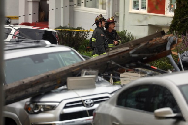 Firefighters look over the scene as a utility pole lays across the hood of a vehicle 10th Avenue on Wednesday, Jan. 4, 2023 in Oakland, Calif. A large tree along with a toppled utility pole blocked the intersection of 10th Avenue and East 28th Street. (Aric Crabb/Bay Area News Group)
